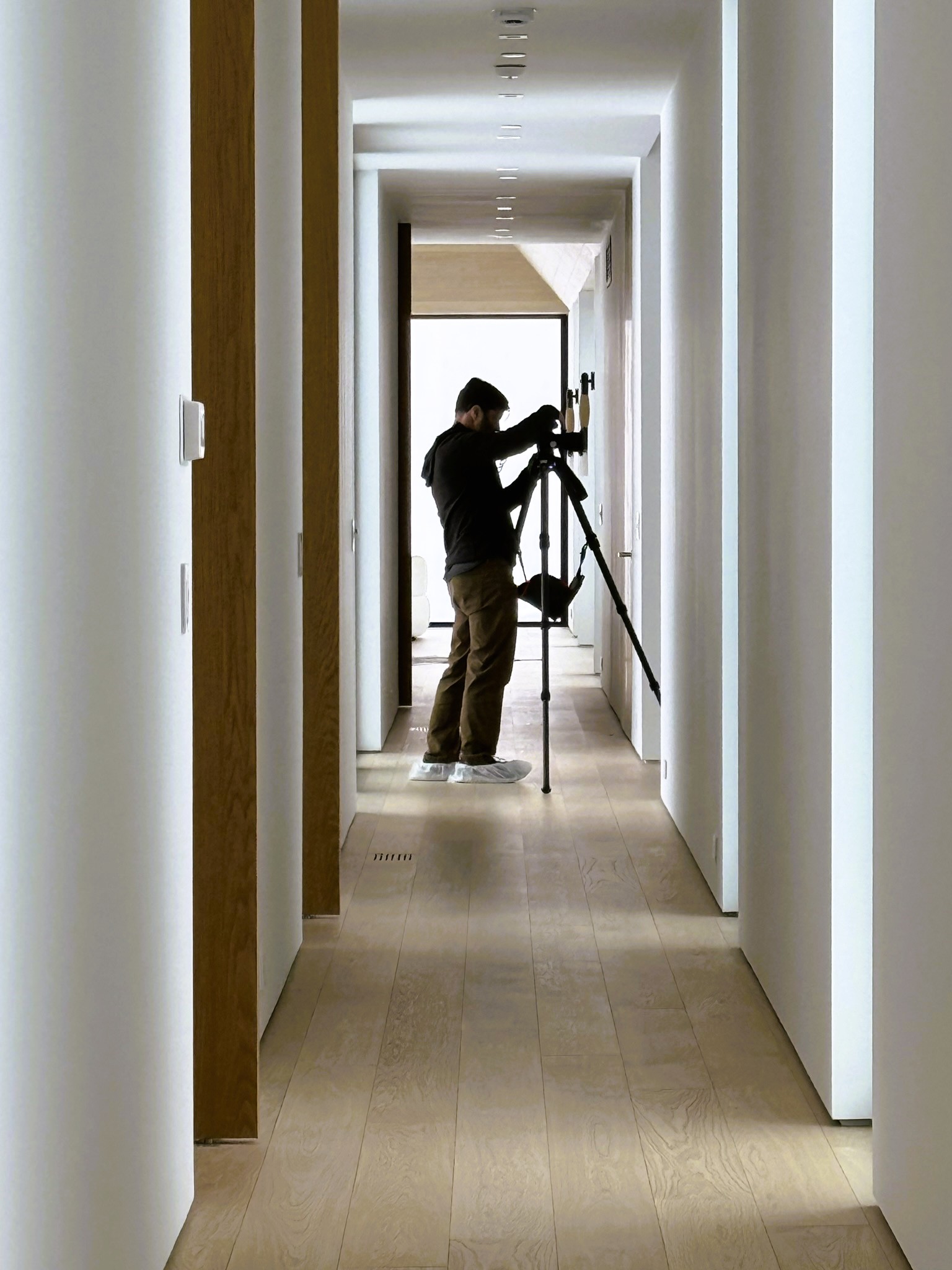 Photographer James Florio documenting the Mountain Ridge residence from a minimalist hallway lined with white walls, oak detailing, and soft winter light.