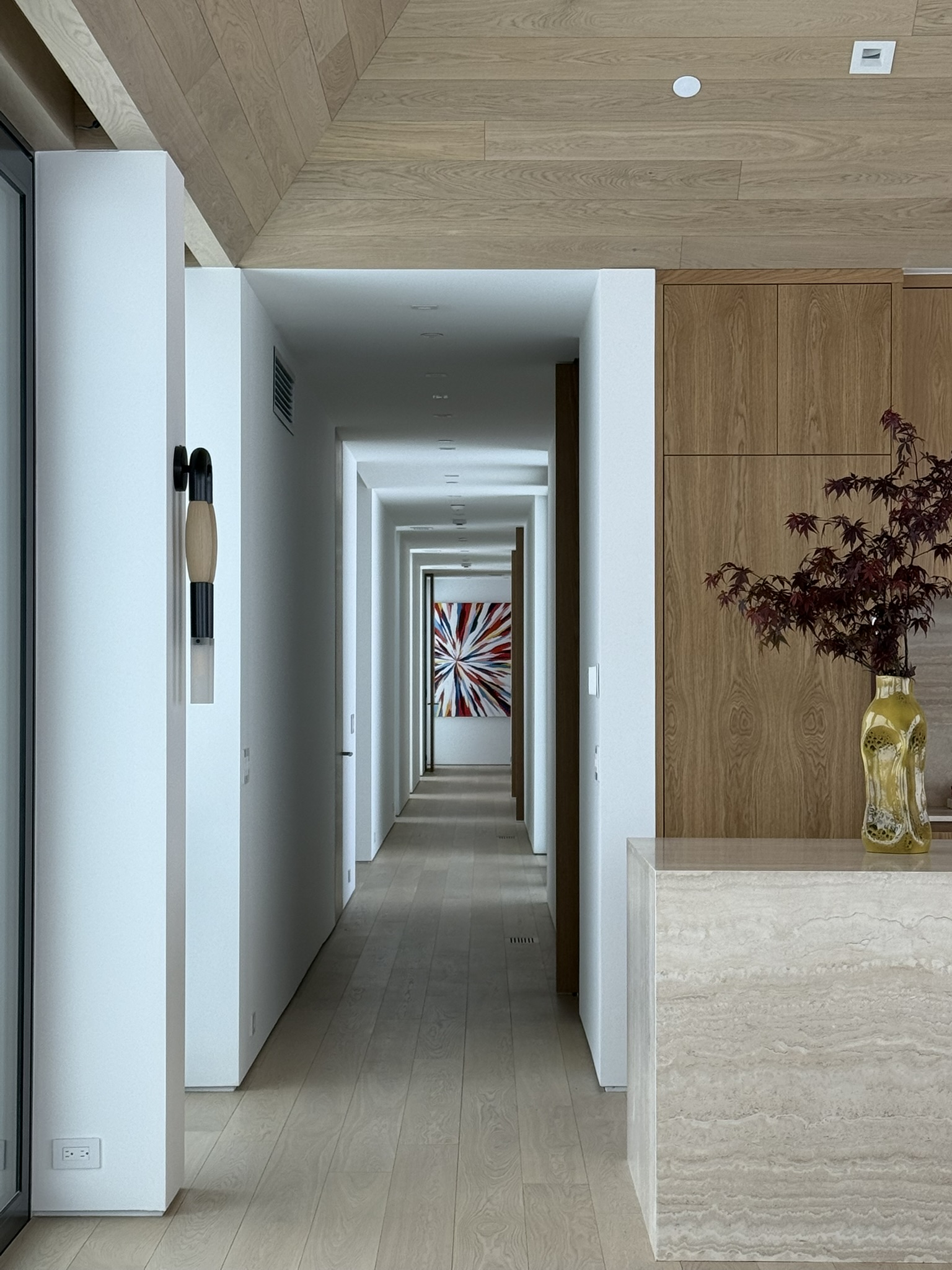 View through the Mountain Ridge kitchen toward a long minimalist hallway illuminated by soft winter daylight and framed by warm oak millwork.