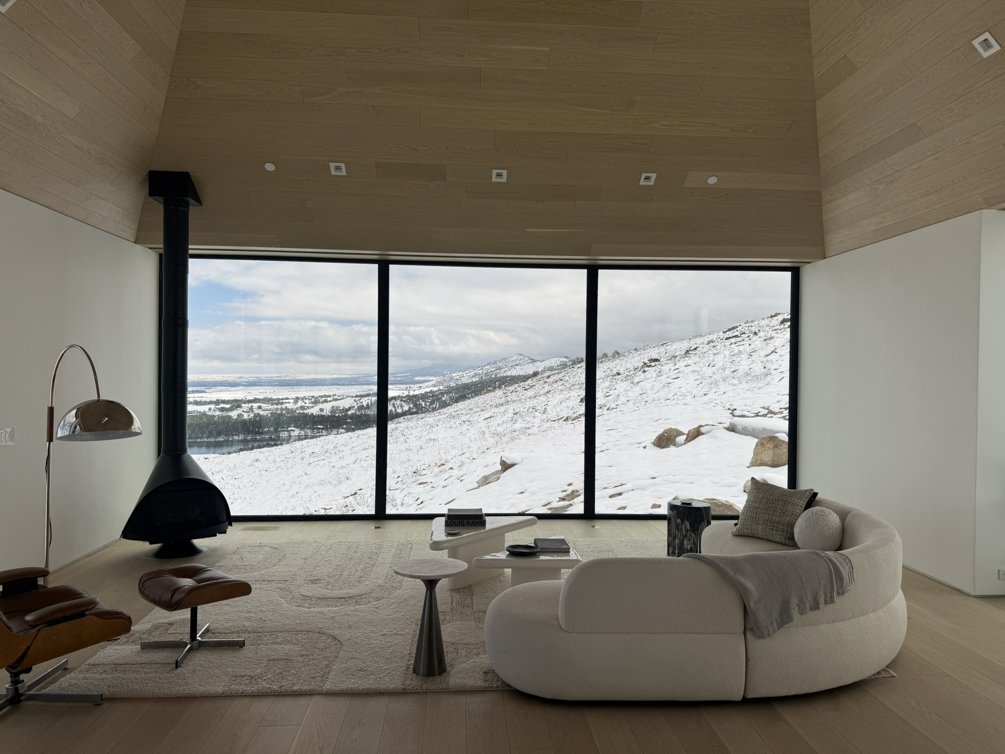 Warm modern living room at Mountain Ridge opening to panoramic snow-covered hillside views through expansive black-framed windows.