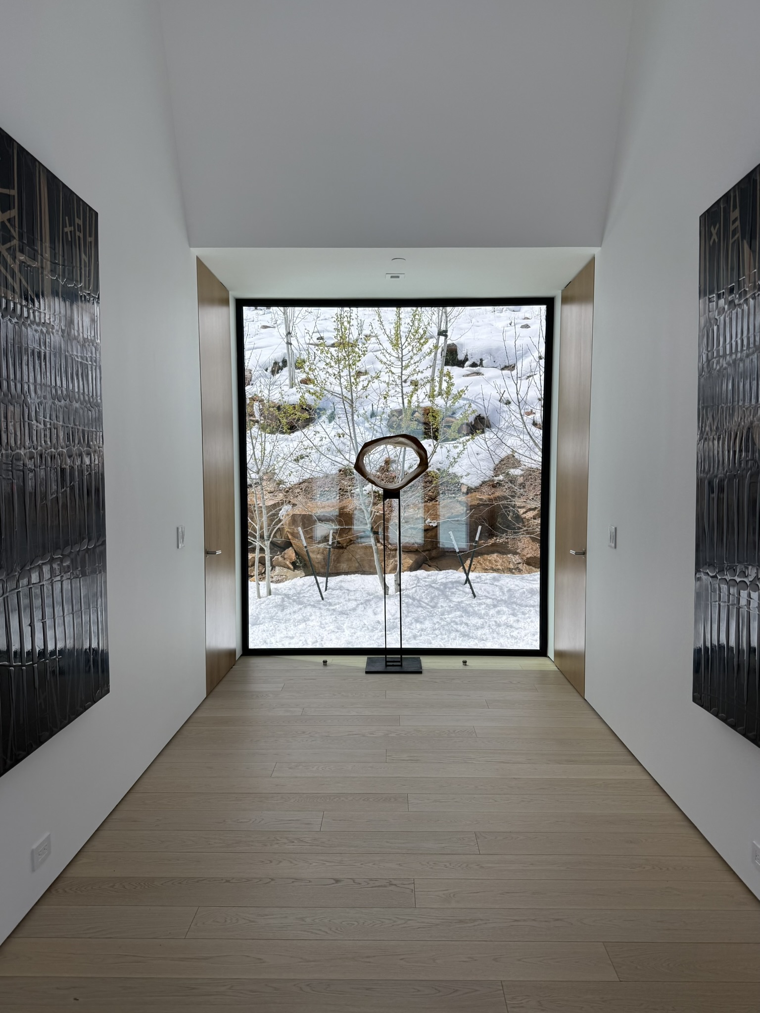 Minimal gallery-style corridor at Mountain Ridge framing a snowy courtyard and sculptural artwork through large black steel windows.
